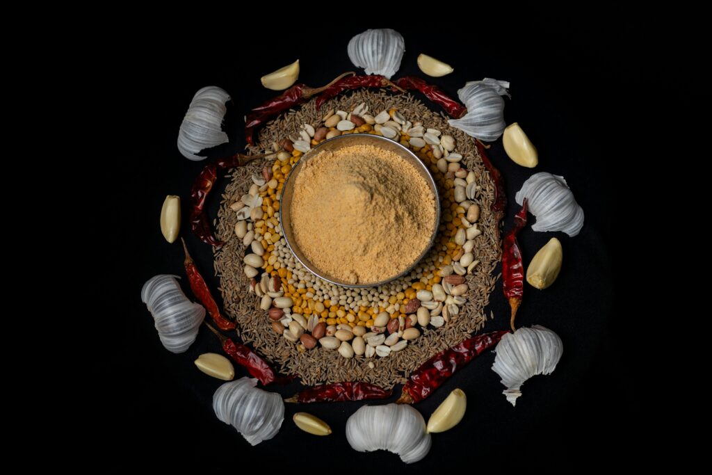 Top view of traditional Indian spices and masala surrounded by garlic and chilies on a dark background.