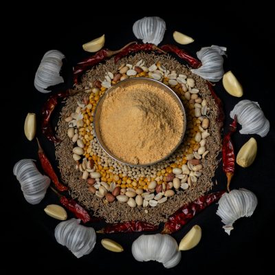 Top view of traditional Indian spices and masala surrounded by garlic and chilies on a dark background.