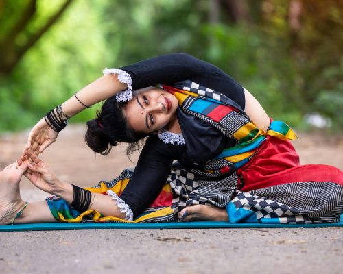 A woman practicing yoga outdoors in colorful attire, showcasing flexibility and mindfulness.