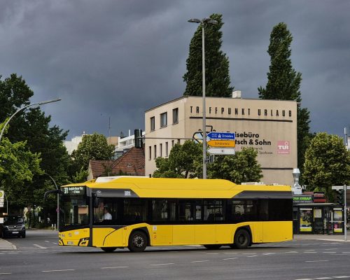 Yellow city bus crossing intersection in Berlin with stormy sky and travel agency background.